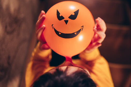 Child playing indoors with Halloween pumpkin balloon in autumn