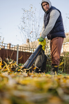 Man using leaf blower for autumn garden cleanup outdoors