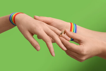 Female hands with rainbow ribbons putting wedding ring on green background. LGBT concept