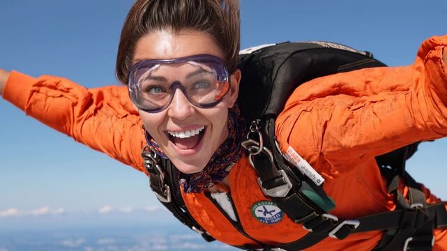 Excited skydiver in orange suit and goggles smiles widely while falling through clear sky capturing extreme adventure adrenaline and fearless travel experience
