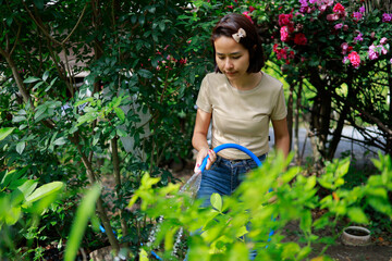 Woman watering plants with a garden hose.