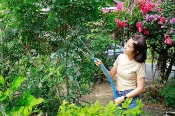 Woman watering plants with a garden hose.