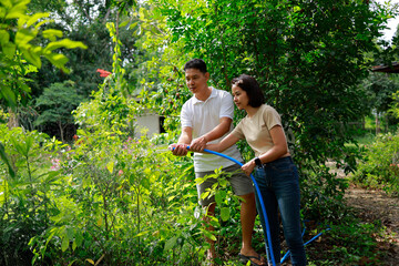 Woman and man watering plants with a garden hose.