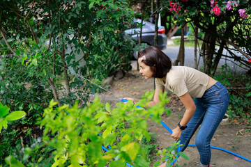 Woman watering plants with a garden hose.