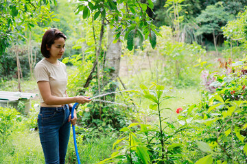 Woman watering plants with a garden hose.