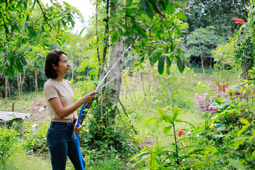 Woman watering plants with a garden hose.