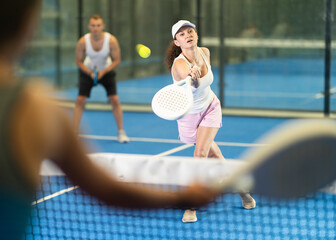 Active woman with racket training on indoor court playing padel game and hitting ball