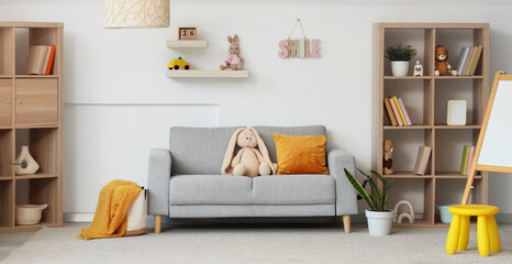 Interior of children's room with sofa, bookshelves, blackboard and different toys near white wall © Pixel-Shot