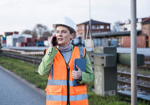 Female logistic manager with safety helmet and tablet making a phone call outdoors