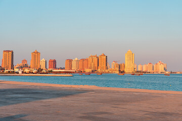 Doha, golden city skyline over calm waters at sunset with beachfront ahead