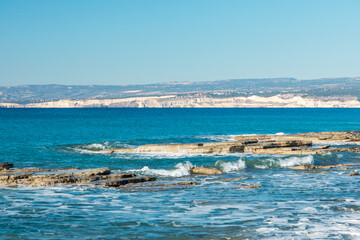 Cyprus, vibrant blue sea with rocky shoreline and distant hills under clear sky
