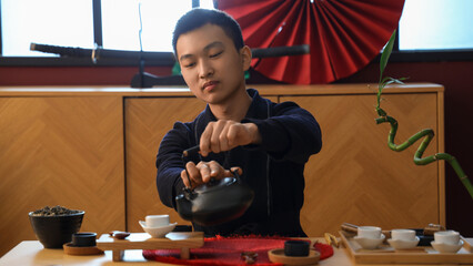 Young Asian man pouring tea at table at home