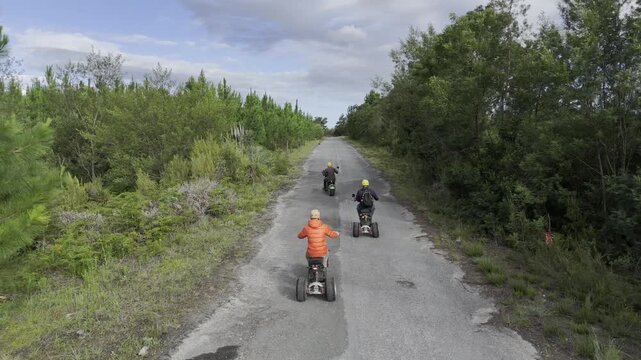 Drone follows three electric scooters touring the pine tree forests at the base of the Tsitsikamma Mountains on a sunny day in Stormsrivier, Eastern Cape, South Africa
