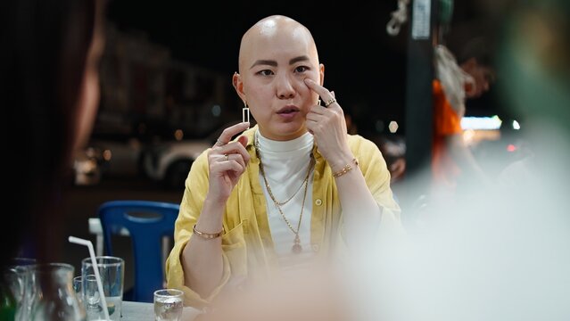 Thai bald woman talking with friends, enjoying moo kra ta street food at night
