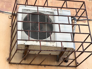 Wall-mounted air conditioner unit with protective metal cage.