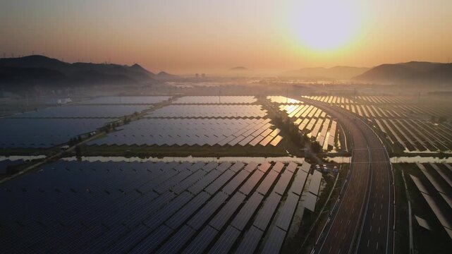 Solar power plant and highway intersecting at sunrise with reflective water surfaces and rolling hills
