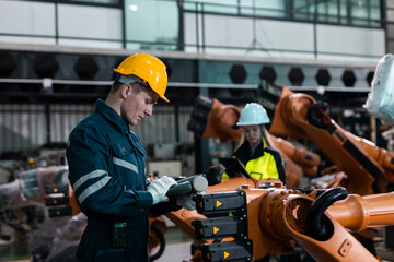 Engineer in safety gear operate and inspect robotic arms using control devices in a modern smart factory. Concept of automation, teamwork, advanced manufacturing technology.