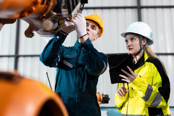 Male and female engineers in safety uniforms collaborate using digital tablets to control robotic arm equipment in smart factory. Concept of teamwork, automation and industry innovation.