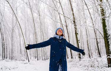 Joyful young woman embracing winter snowfall outdoors in nature. 