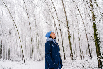 Woman enjoying peaceful winter moment in snowy forest. Woman looks at falling snowflakes.