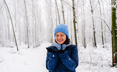 Young woman enjoying winter snowfall outdoors in forest. Woman looking at snowflakes on her gloves.