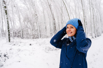Joyful young woman enjoying snowfall in winter forest.