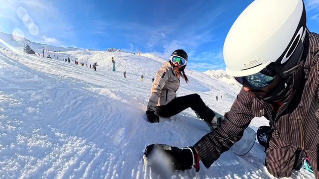 Young couple in ski gear taking a break and talking on a crowded snowy slope during a beautiful sunny day, with majestic snow covered mountains filling the breathtaking background view