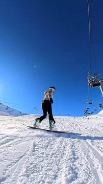 Young snowboarders enjoying a sunny day on the slopes, skillfully gliding down a perfectly groomed piste under a clear blue sky, with a chairlift overhead in a famous mountain resort