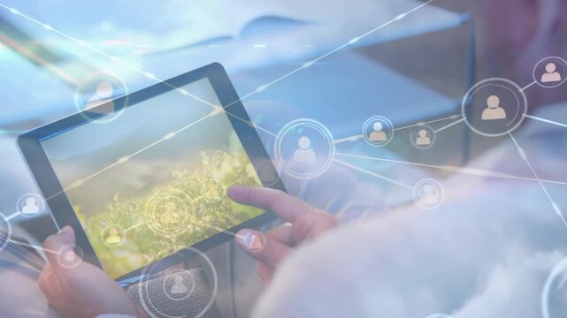Network of profile icons against mid section of a person using digital tablet against clouds in sky
