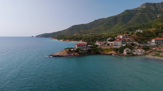 Aerial drone orbit shot circling the rugged coastline and turquoise Aegean Sea near Kinira village on the forested island of Thasos, Greece.