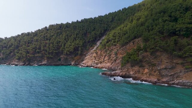 Aerial drone tracking shot panning low above the turquoise water along the pristine Kinira Beach and the densely forested coast of Thasos Island, Greece.