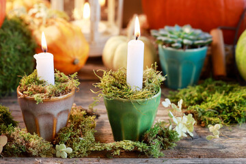Classic autumn decorations with pumpkins, candles and moss on wooden table.