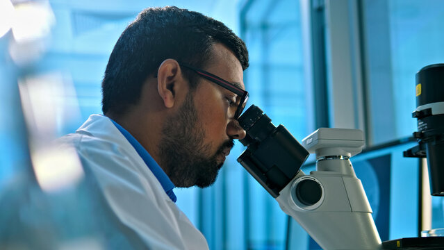 A focused researcher in a lab coat examines a specimen under a microscope, highlighting precision and scientific inquiry in a modern lab. The scene emphasizes meticulous observation and analysis.