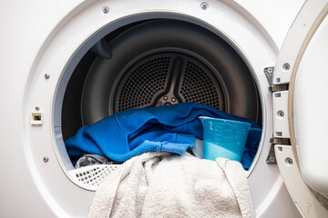 Front loading washing machine with blue clothes and towels inside the drum, open door view, household laundry routine, cleanliness, hygiene and domestic appliance usage at home.