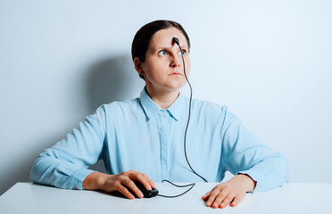 Person in blue shirt with mouse cable on forehead at office desk