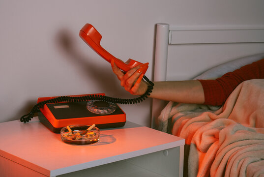Hand with false nails holding retro phone at night on hotel bedside table