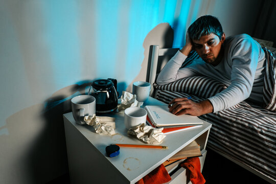 Man suffering insomnia with coffee and creative burnout at night in bedroom