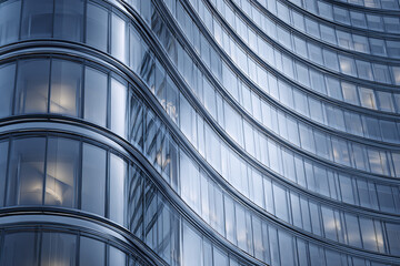Obraz premium Modern curved glass facade of office building reflects soft light, creating sleek and elegant architectural design with smooth lines and transparent windows