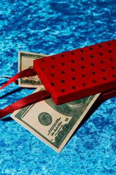 Red gift box with ribbon and fake dollar bills on blue velvet