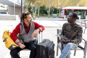 Two friends with backpacks and suitcases waiting at the bus station