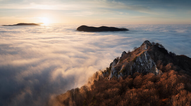Sunset with clouds, sun rays, and misty valleys witn forest, mountain and peak nature landscape.