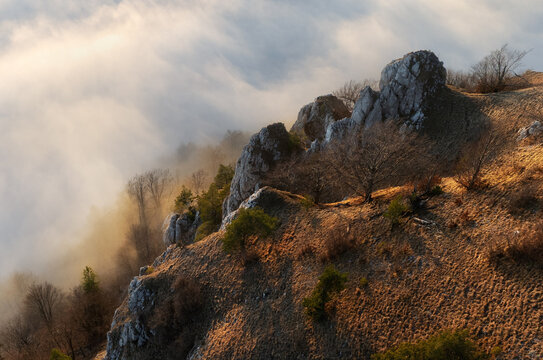 Sunset with clouds, sun rays, and misty valleys witn forest, mountain and peak nature landscape.