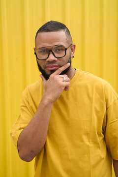 Portrait of confident man in yellow shirt reflecting with hand on chin
