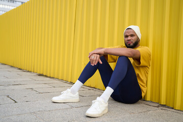 Young man in casual outfit sitting by yellow wall outdoors in calm