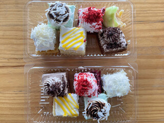 Assorted small cake cubes with colorful toppings arranged in plastic container, homemade dessert concept