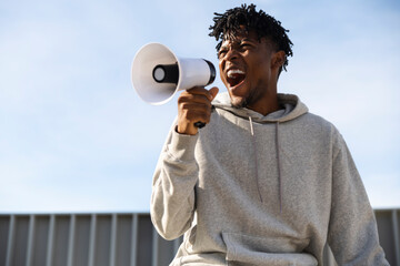 Man in grey tracksuit shouting with megaphone outdoors