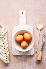 Braune Eier in einer Sch&uuml;ssel, ein Kochl&ouml;ffel und ein Schneebesen auf einem Stein Hintergrund. Draufsicht, Fr&uuml;hst&uuml;ck.