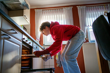 Teenager boy baking pizza at home in oven.