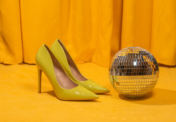 Yellow high heels and disco ball on yellow background for party theme