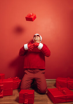 Santa wearing red clothes kneeling and tossing Christmas gift indoors